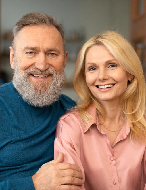 Smiling middle-aged couple posing together indoors in casual clothing against neutral background.
