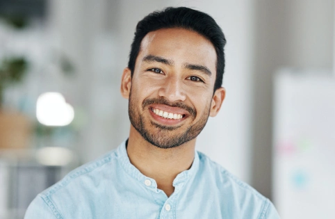Smiling male dental professional in light blue shirt against blurred office background