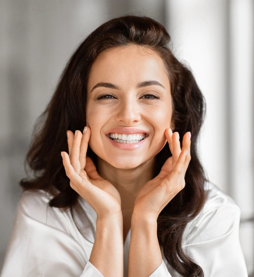 Smiling woman with hands near face in bright dental office setting, representing friendly dental care professional.