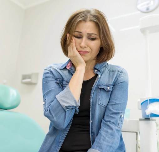 Woman in denim shirt smiling thoughtfully in modern dental office setting.