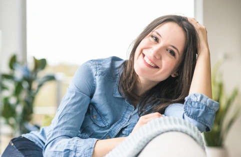 Smiling woman in denim shirt relaxing indoors with plant in background