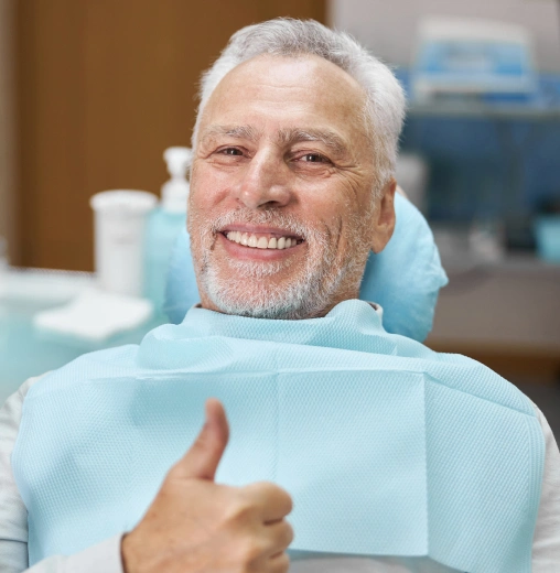 Smiling mature man in dental bib giving thumbs up in dental office setting.