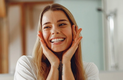 Smiling woman with hands on face in bright dental office setting, expressing happiness and satisfaction.