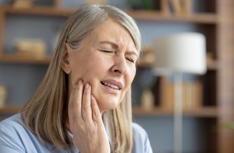 Woman holding her cheek in discomfort, appearing to experience dental pain in a modern dental office setting.