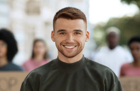 Smiling man in dark shirt at outdoor dental or medical event with blurred crowd background.