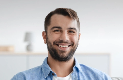 Smiling male dental professional in blue shirt against modern office background.