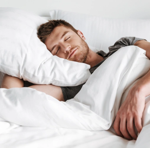Man sleeping peacefully in bed with white pillows and bedding.