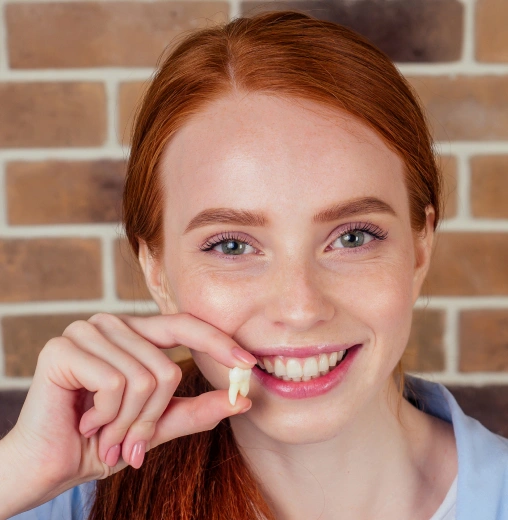 Smiling redhead girl holding dental floss against brick wall background.