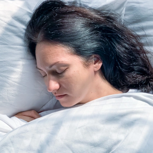 Woman sleeping peacefully on white pillow and bedding, eyes closed.