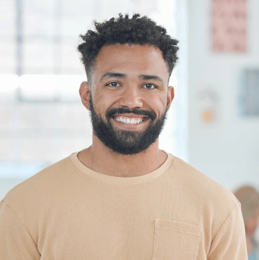 Smiling man in tan shirt against blurred office background, professional headshot.