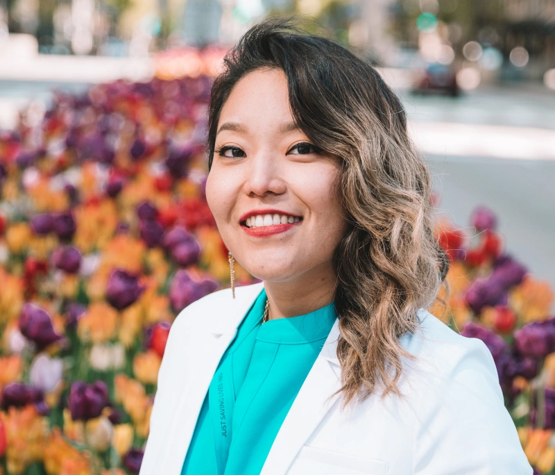 Professional outdoor headshot of Dr. Ariee Jung smiling in a white lab coat.